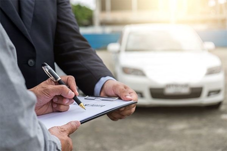 A man signing paperwork with a car in the background